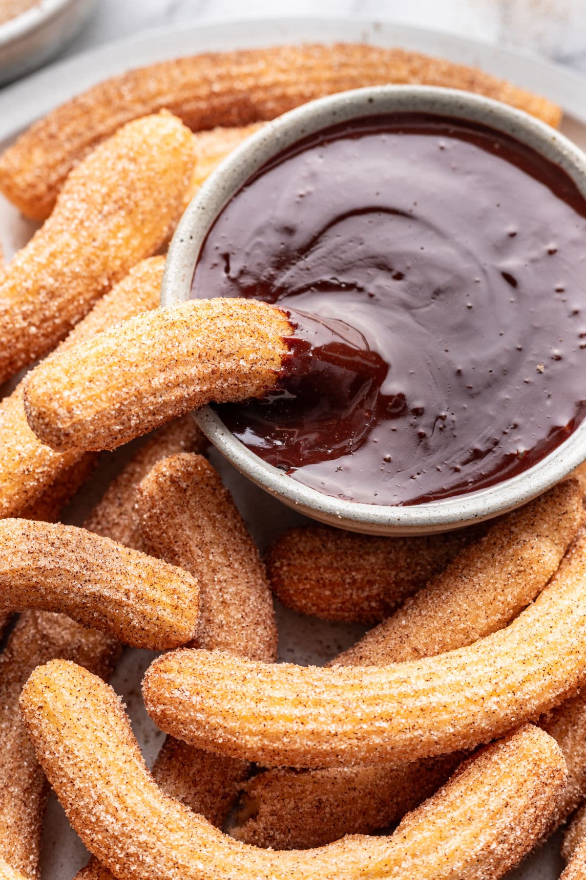 Close up of a churro in a dish of chocolate dipping sauce surrounded by other churros. 