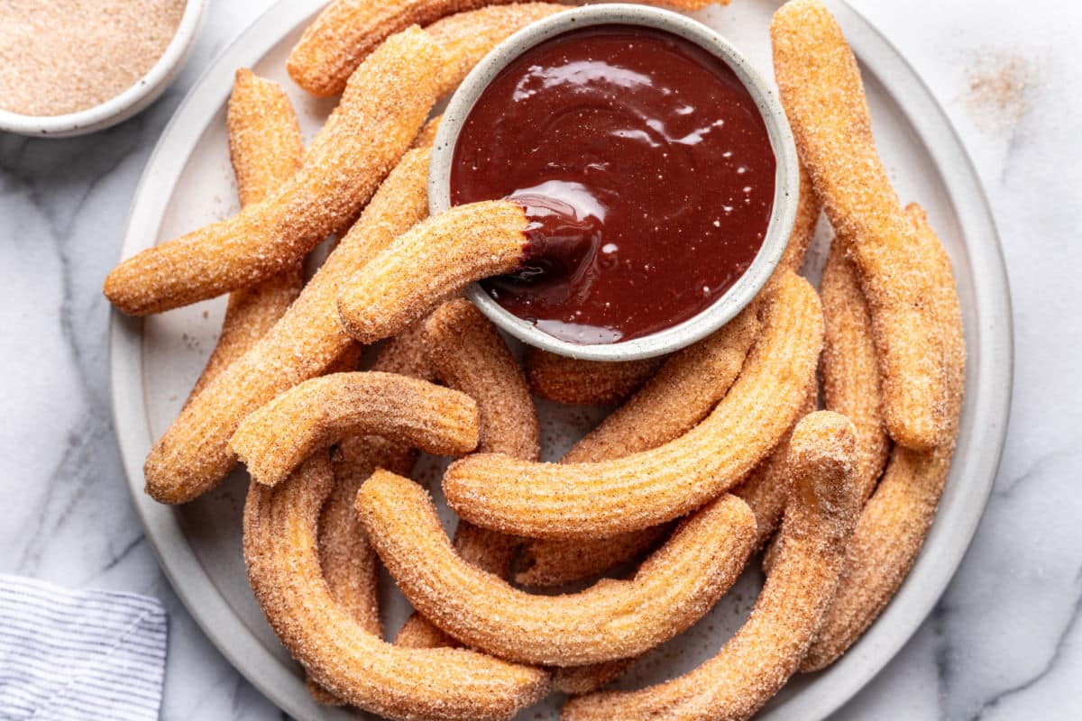 A churro in a dish of chocolate dipping sauce on a platter of churros. 