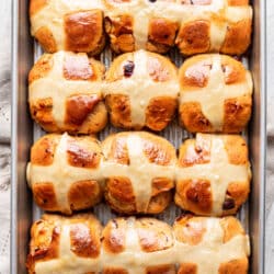 A pan of hot cross buns next to a kitchen cloth.