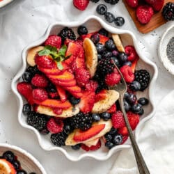 A scalloped dish of Poppy seed fruit salad next to fresh berries.