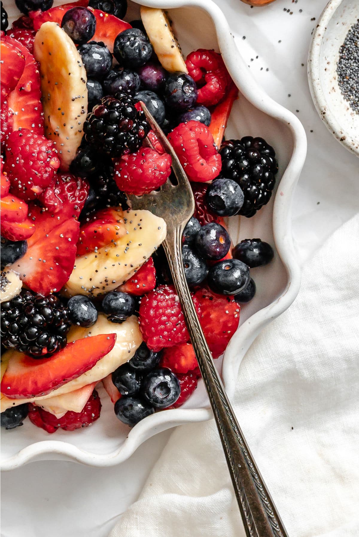 a scalloped dish of poppy seed fruit salad with a silver fork in it.
