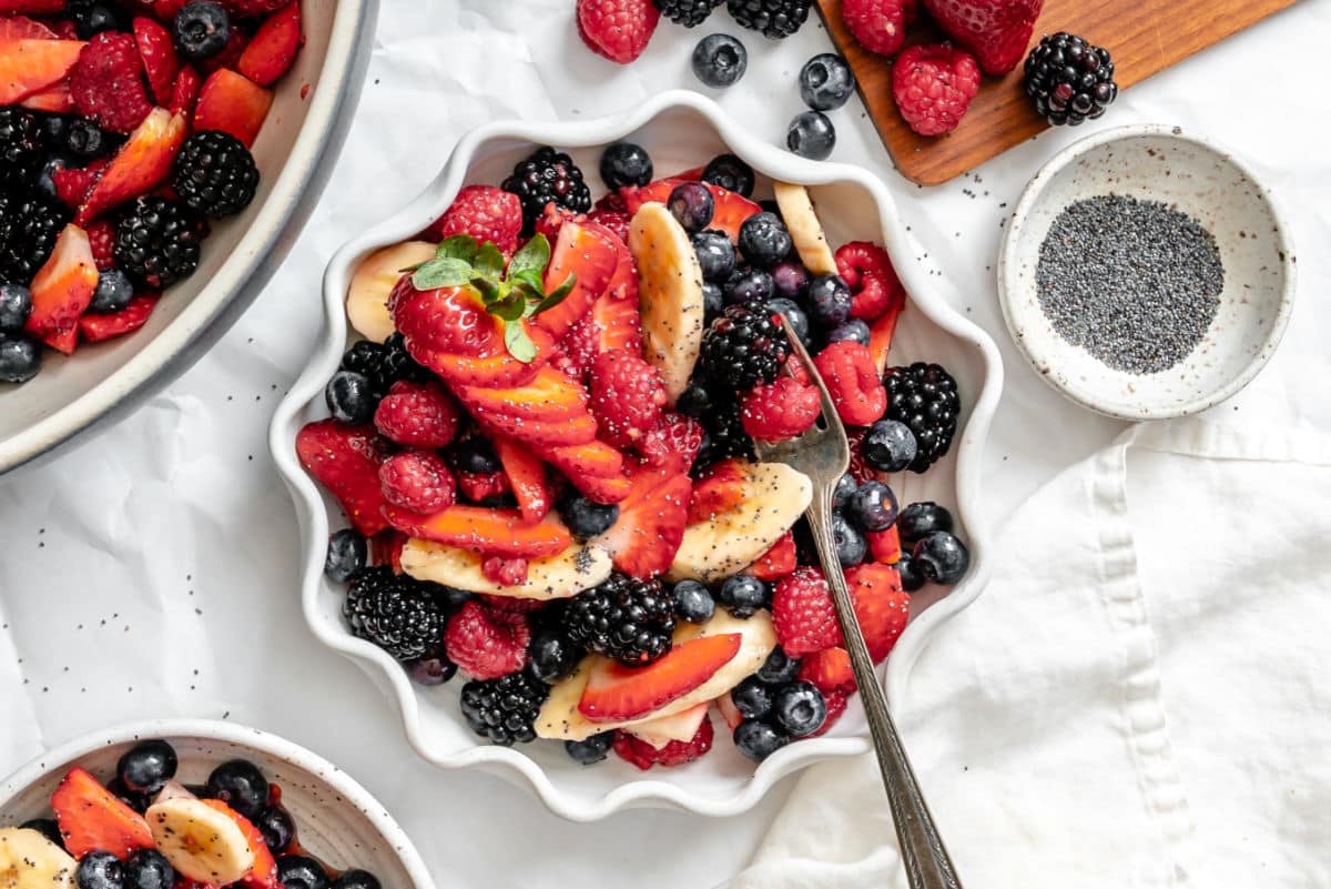 Poppy seed fruit salad in a scalloped dish next to a dish of poppy seeds.