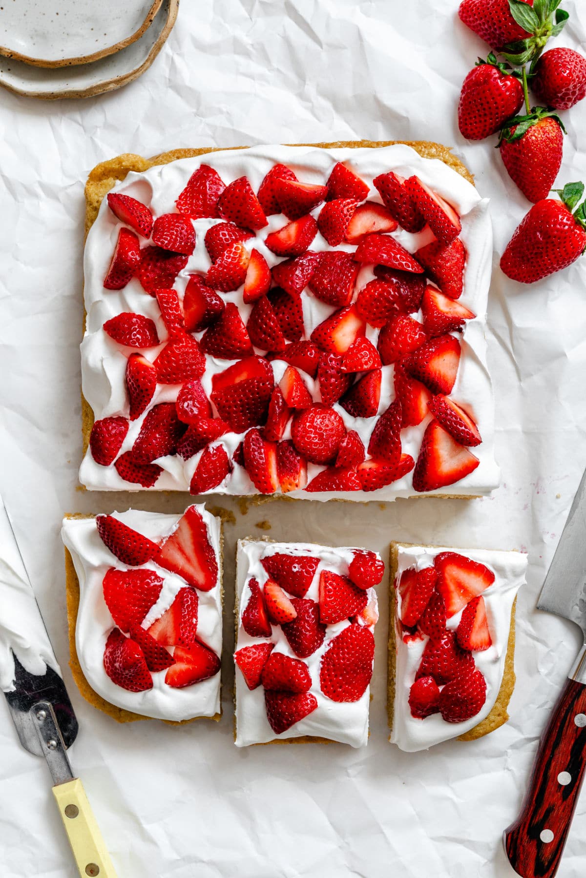 Three cut strawberry shortcake bars next to the entire pan of bars.