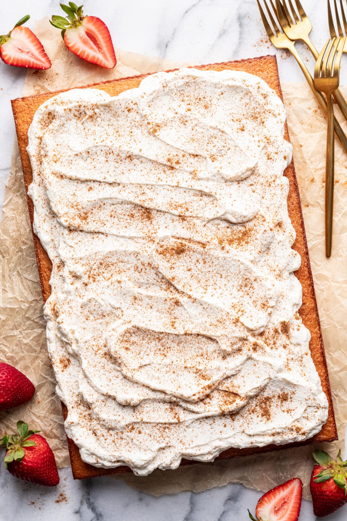 A tres leches cake on a piece of parchment paper next to fresh strawberries.
