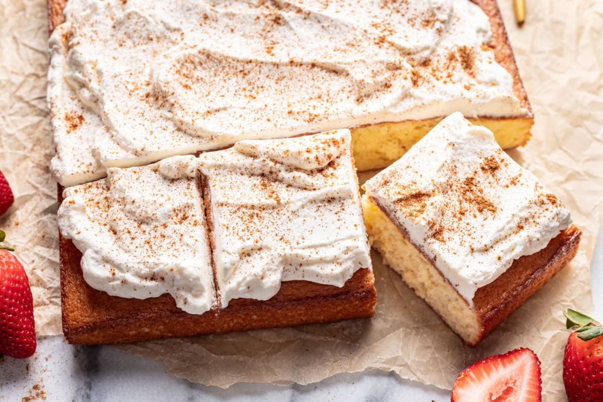 Three pieces of tres leches cake with one at an angle next to the entire cake.