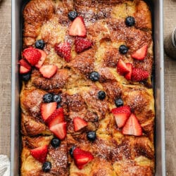 A pan of croissant baked French toast topped with sliced strawberries and blueberries.