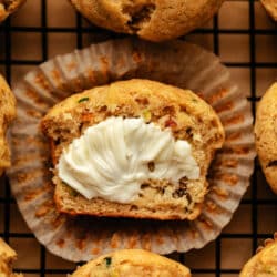 A buttered half zucchini muffin on a cupcake wrapper.