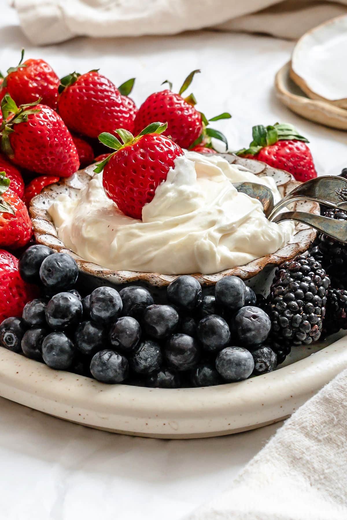 A strawberry and a silver spoon in a dish of marshmallow fruit dip.