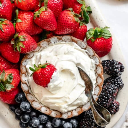A dish of marshmallow fruit dip surrounded by fresh strawberries and blueberries.