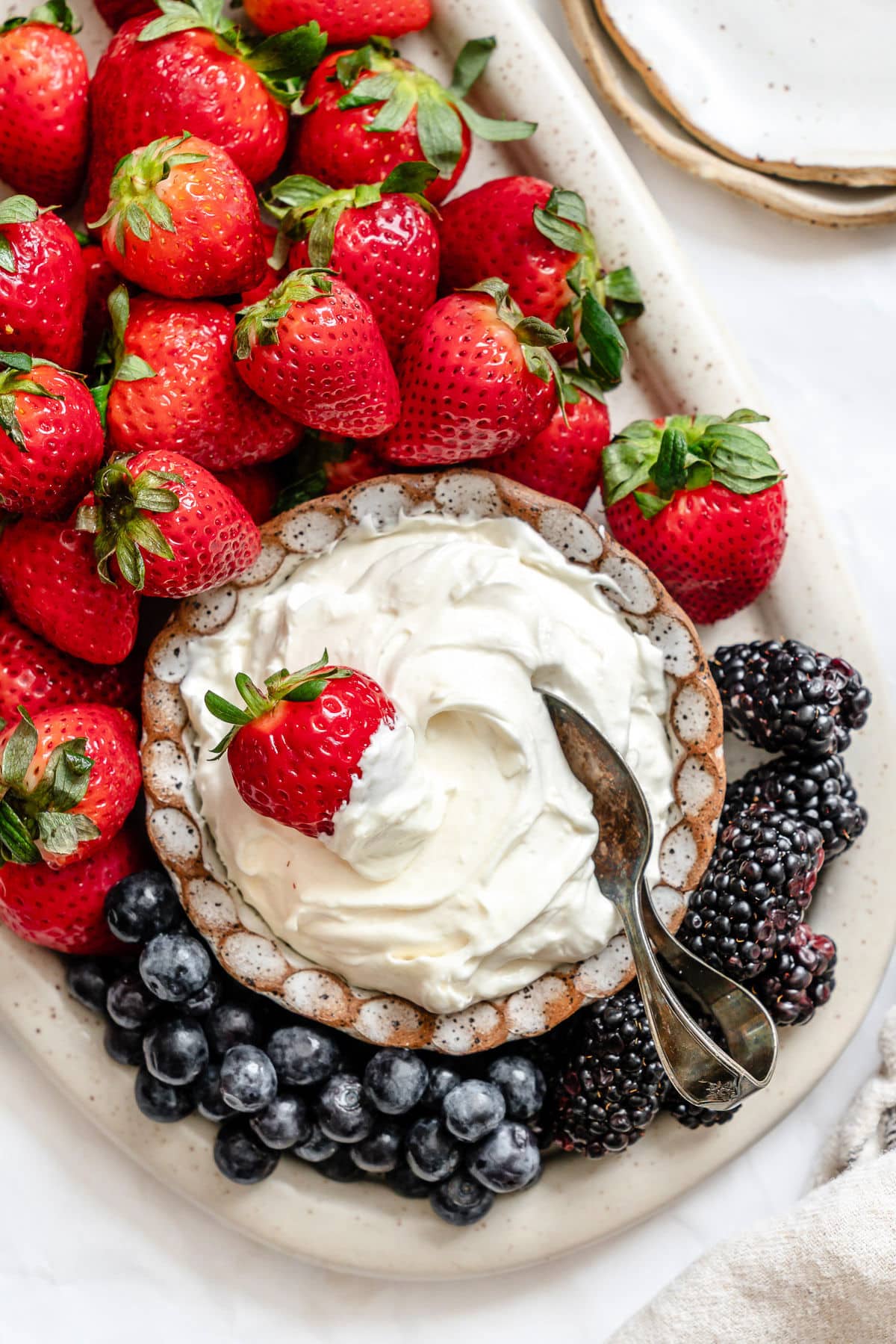 A dish of marshmallow fruit dip surrounded by fresh strawberries and blueberries.