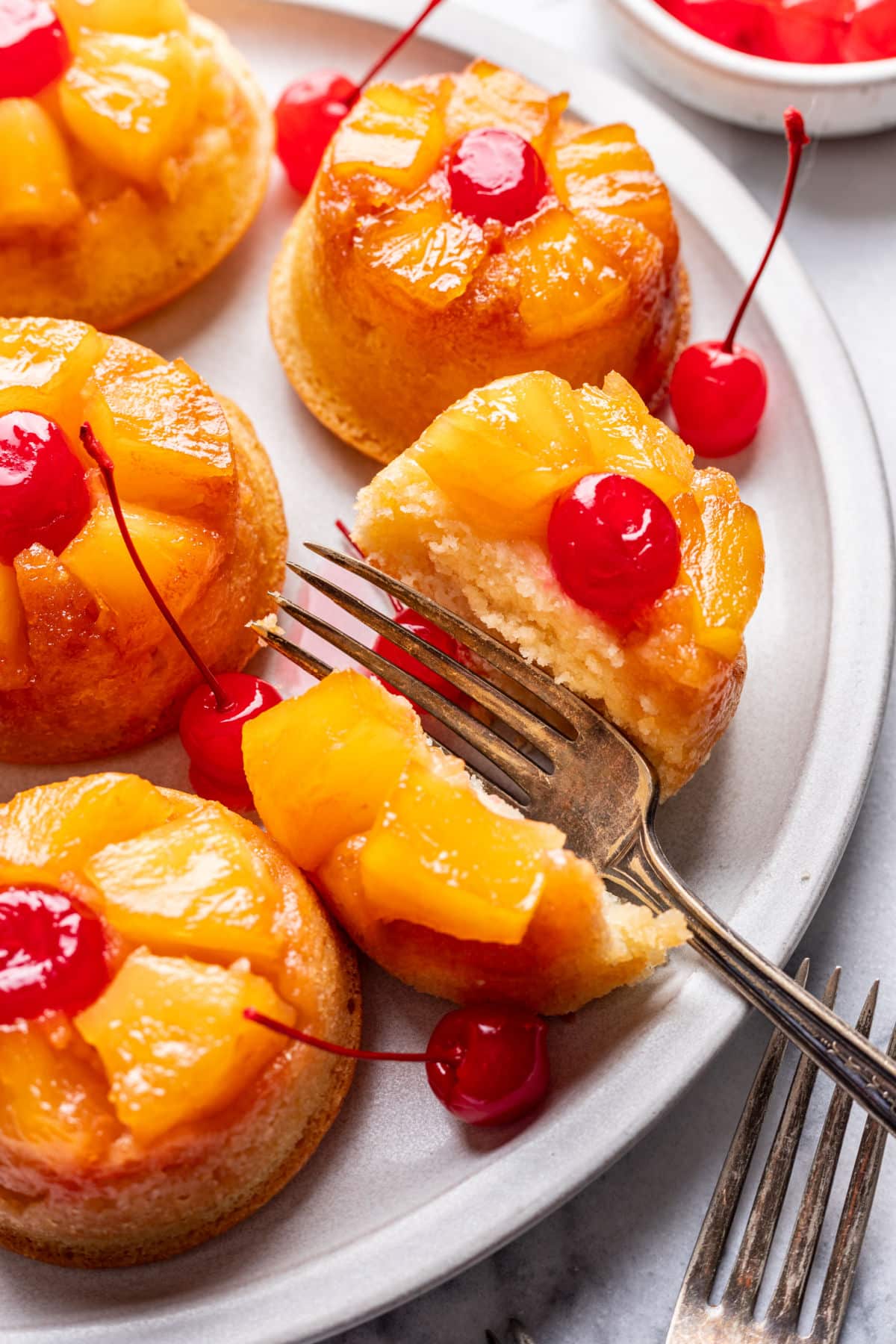A fork cutting a bite from a pineapple upside down cupcake.