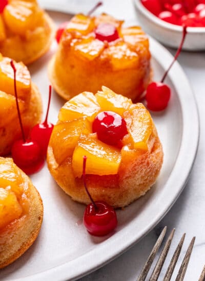 A pineapple upside down cupcake surrounded by maraschino cherries on a platter.