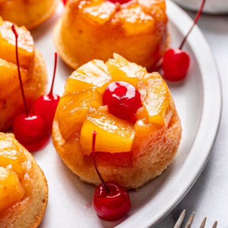 A pineapple upside down cupcake surrounded by maraschino cherries on a platter.