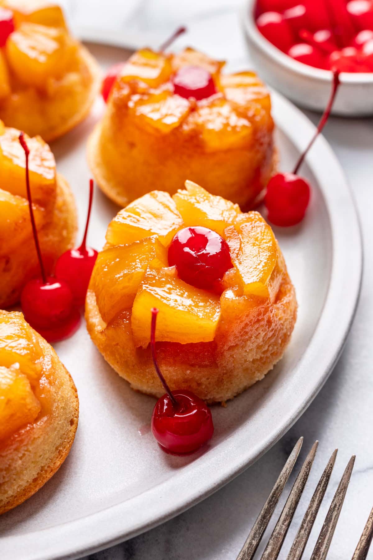 A pineapple upside down cupcake surrounded by maraschino cherries on a platter.
