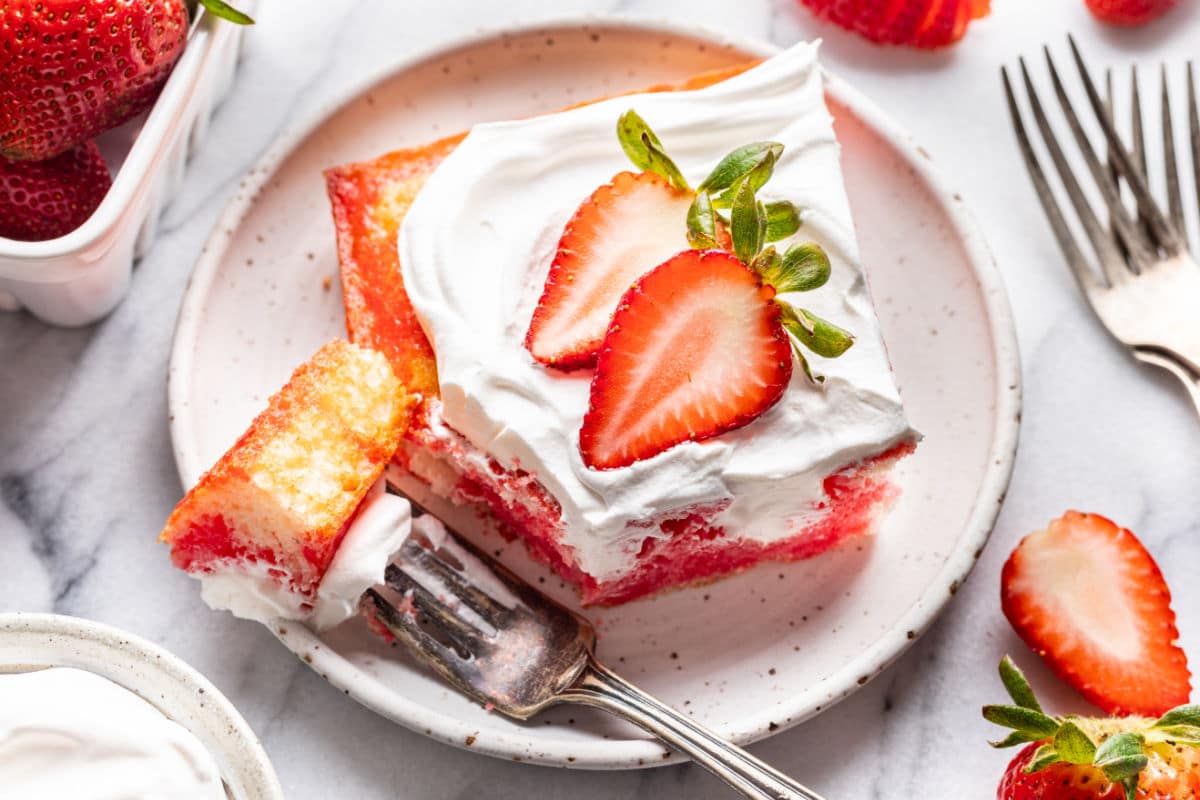 A piece of jello poke cake with a bite of the cake on a fork. 
