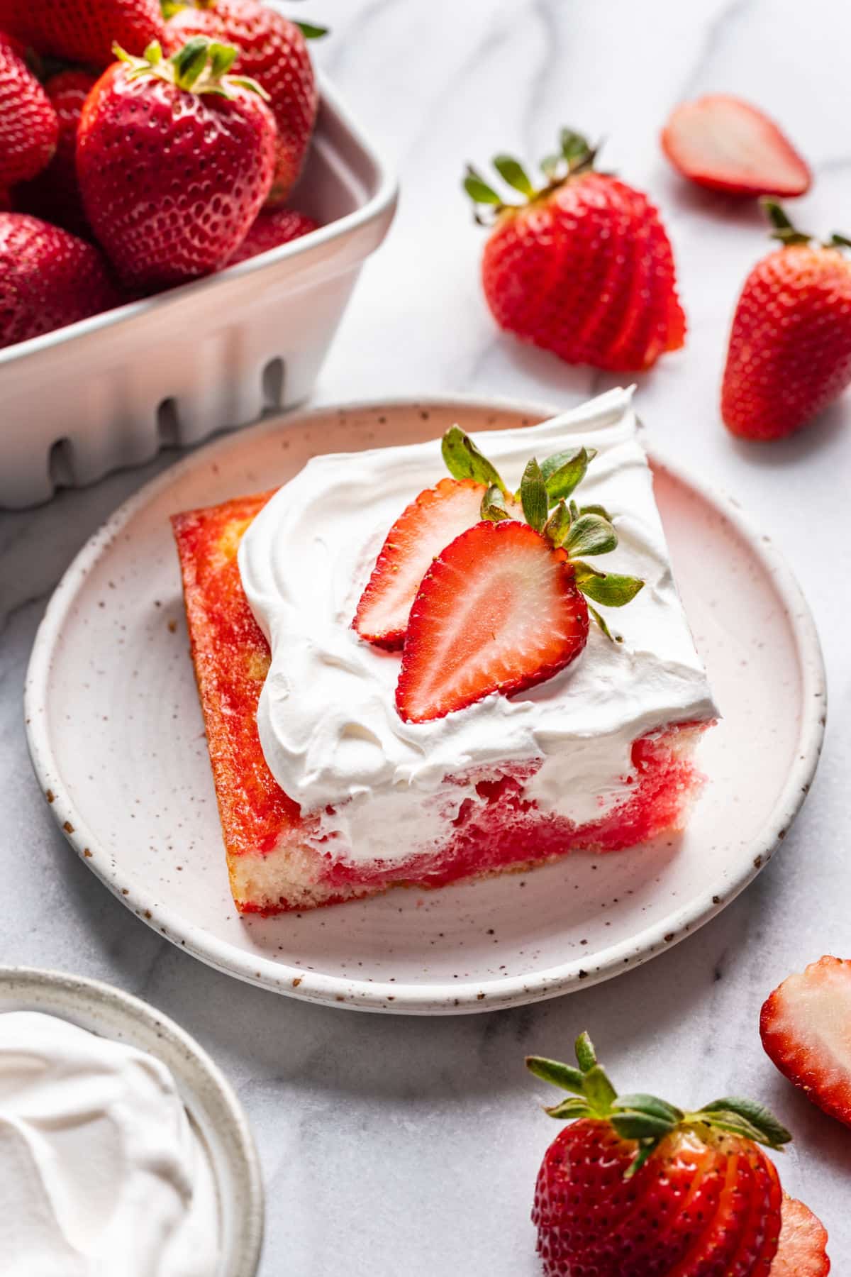 A slice of Jello Poke cake on a plate surrounded by fresh strawberries. 