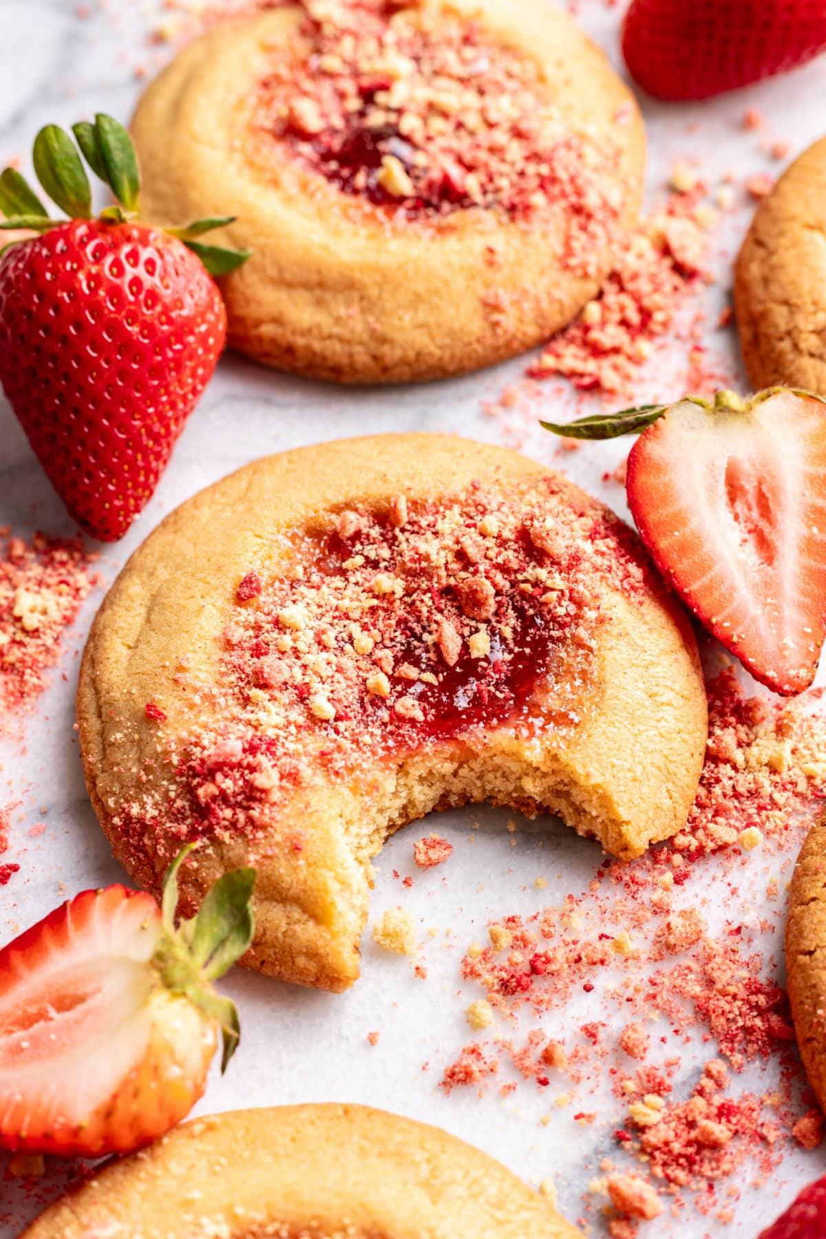 A strawberry shortcake cookie with a bite missing next to more cookies.
