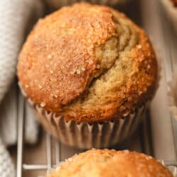 A row of small batch banana muffins on a wire rack next to a cream kitchen linen.