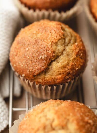 A row of small batch banana muffins on a wire rack next to a cream kitchen linen.