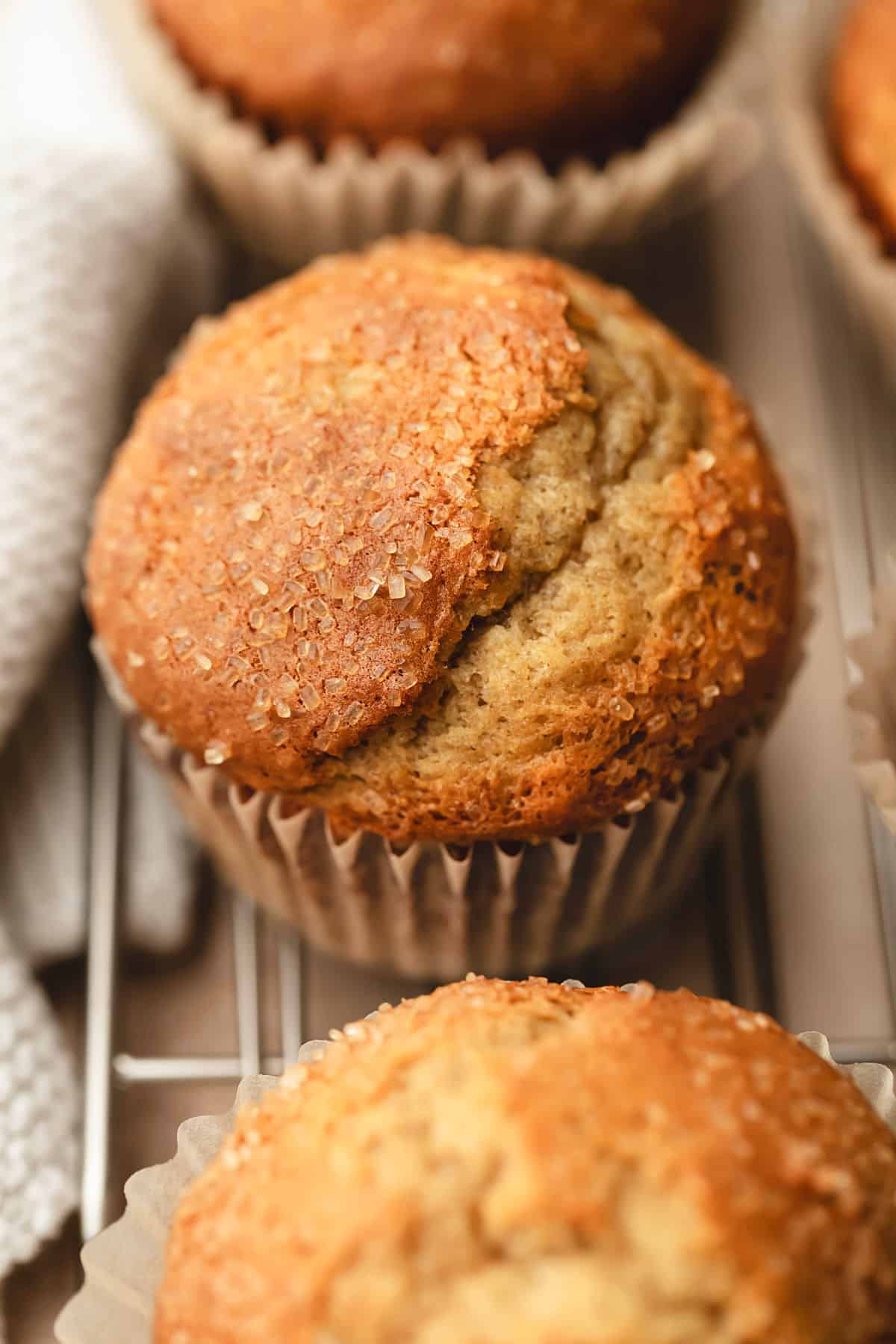 A row of small batch banana muffins on a wire rack next to a cream kitchen linen.