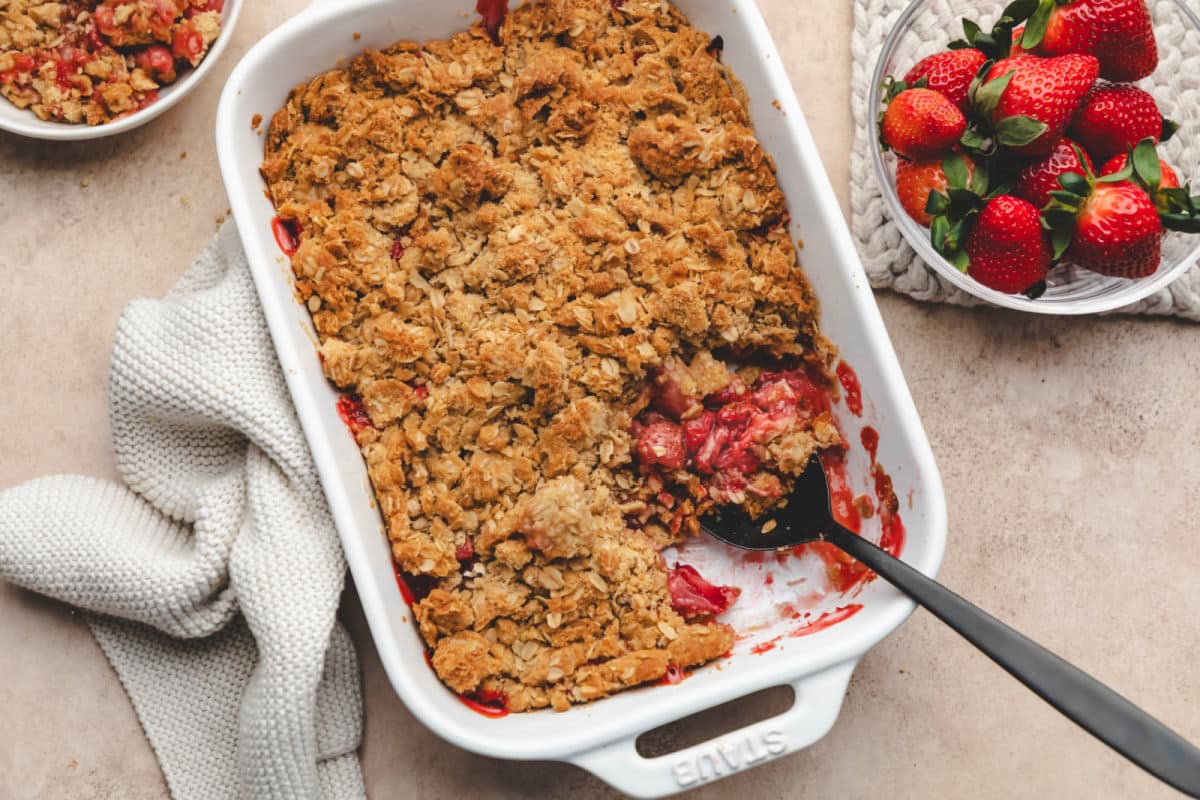 Un plat de croustillant aux fraises à côté d'un bol de fraises fraîches.