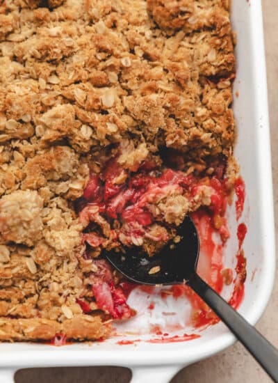 A black spoon holding a scoop of strawberry crisp in a white pan.