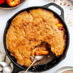 A spoon scooping up brown sugar peach cobbler from a cast iron skillet.