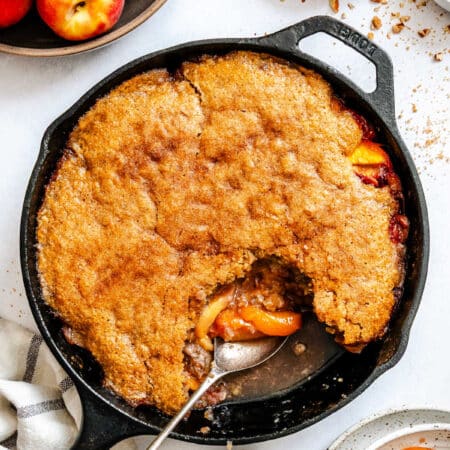 A spoon scooping up brown sugar peach cobbler from a cast iron skillet.