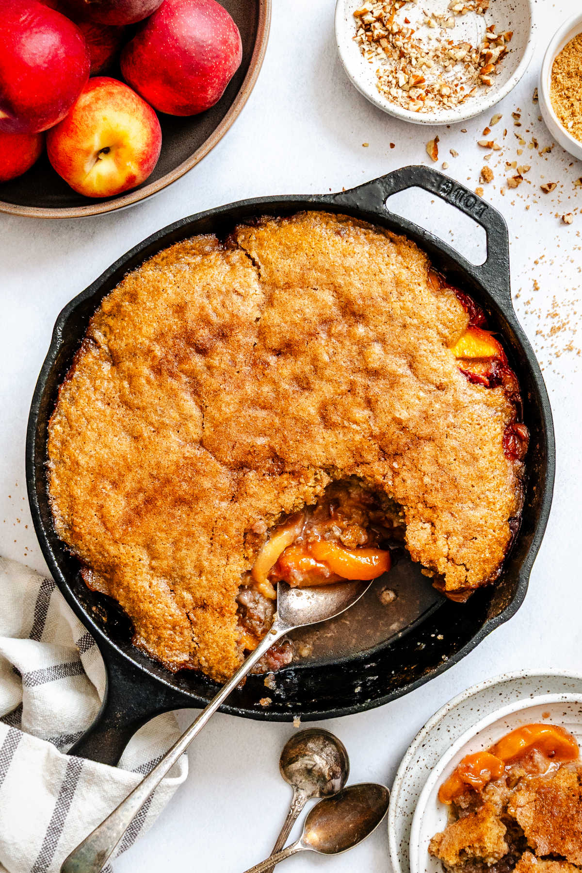 A spoon scooping up brown sugar peach cobbler from a cast iron skillet.