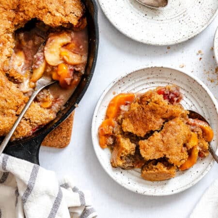 A plate of brown sugar peach cobbler next to the skillet.