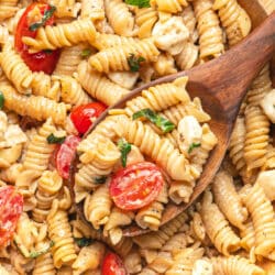 A wooden spoon holding a scoop of caprese pasta salad in the bowl.