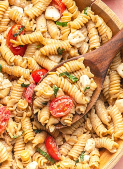 A wooden spoon holding a scoop of caprese pasta salad in the bowl.