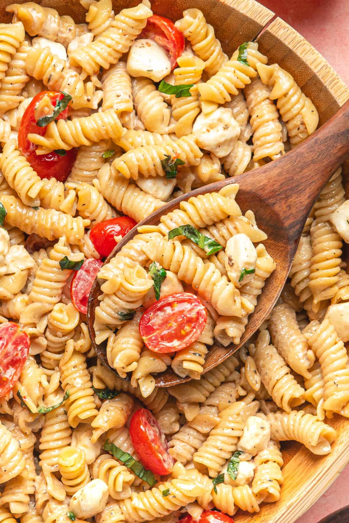 Une cuillère en bois tenant une portion de salade de pâtes caprese dans un bol.