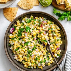 A dish of corn salsa next to tortilla chips and limes.
