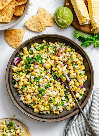A dish of corn salsa next to tortilla chips and limes.