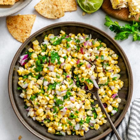 A dish of corn salsa next to tortilla chips and limes.