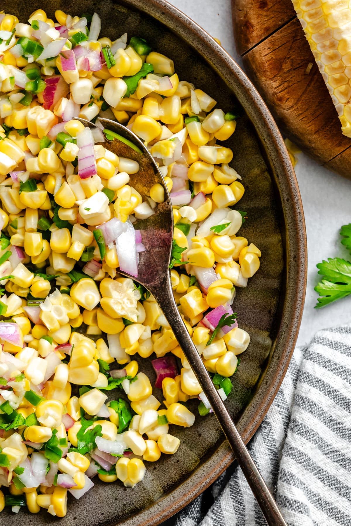 A spoon holding a scoop of fresh corn salsa in a dish of salsa.