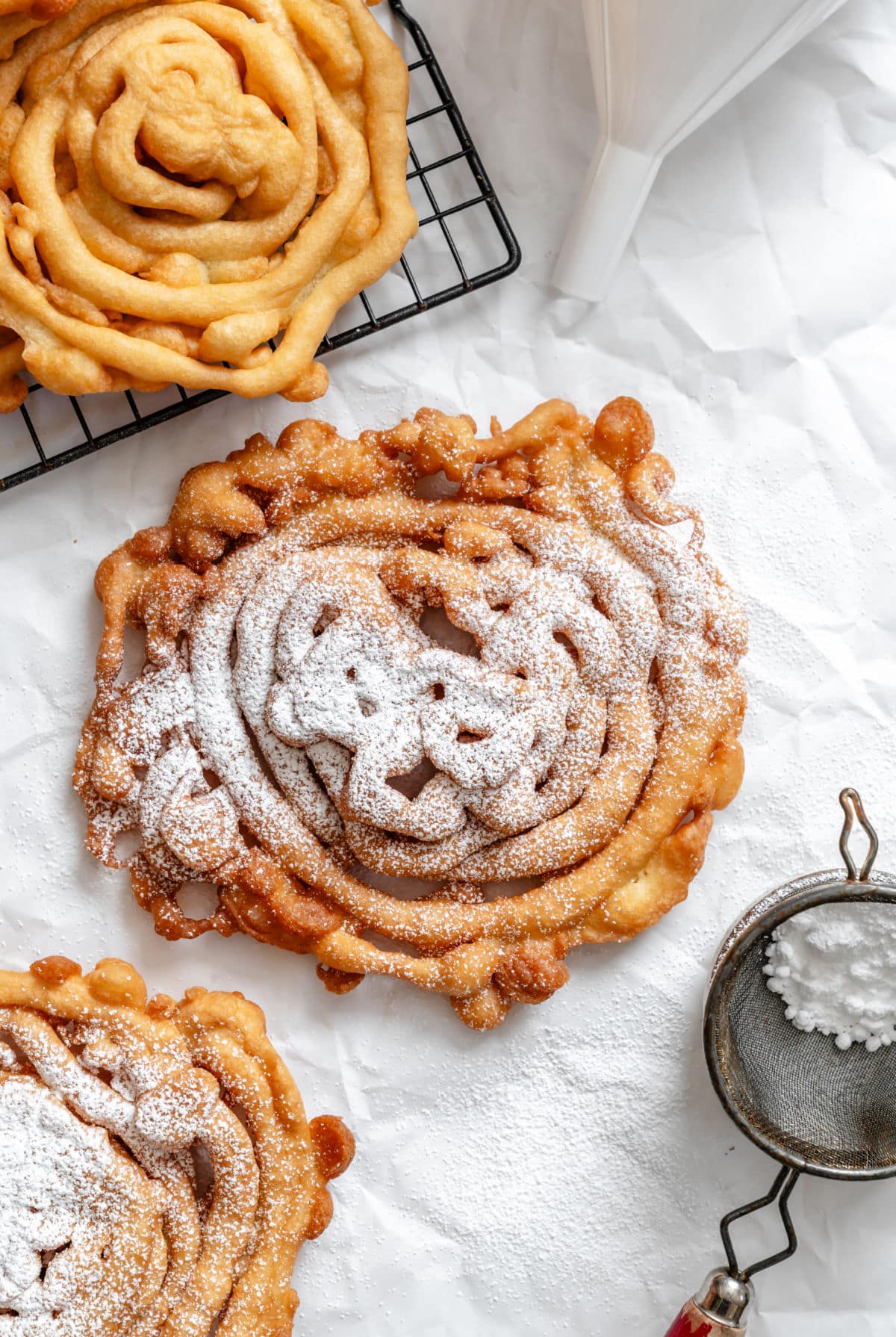 A funnel cake topped with powdered sugar next to a powdered sugar sifter.