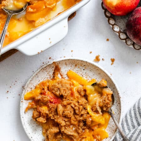 A plate of peach crumble next to the baking pan.