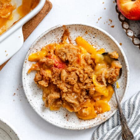A plate of peach crumble between a bowl of peaches and a dish of peach crumble.