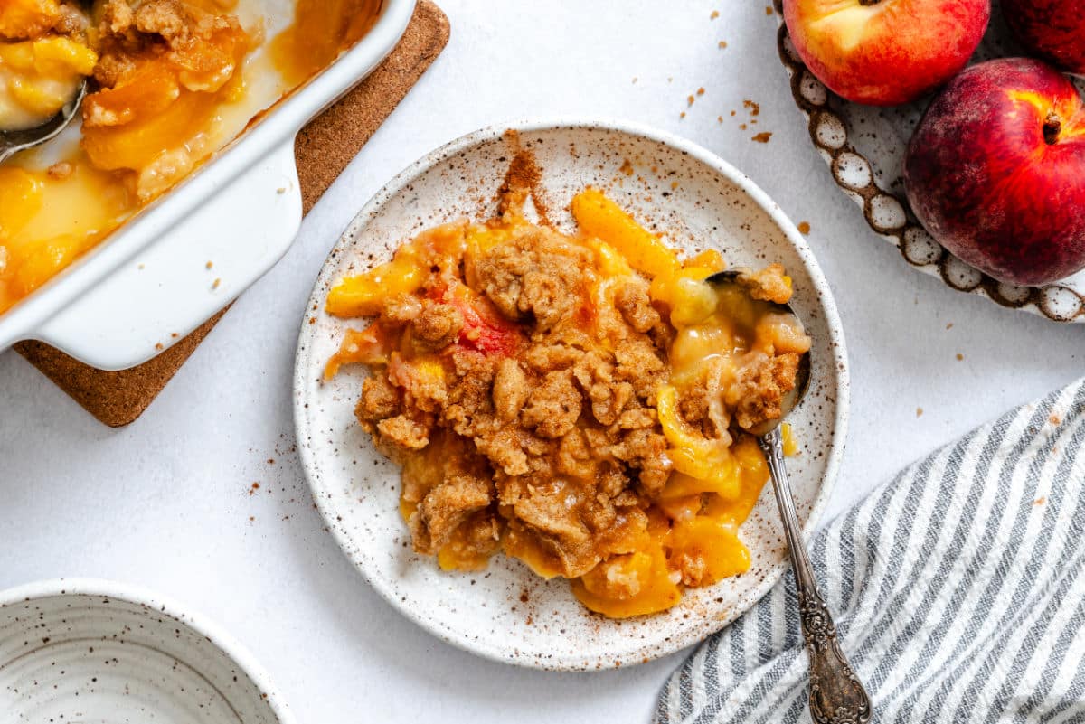 A plate of peach crumble between a bowl of peaches and a dish of peach crumble.