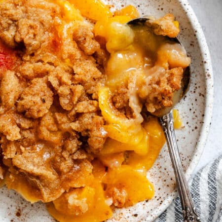 Close up photo of a plate of peach crumble with a spoon in it.