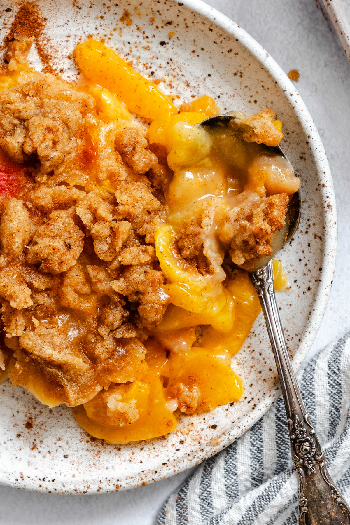Close up photo of a plate of peach crumble with a spoon in it.