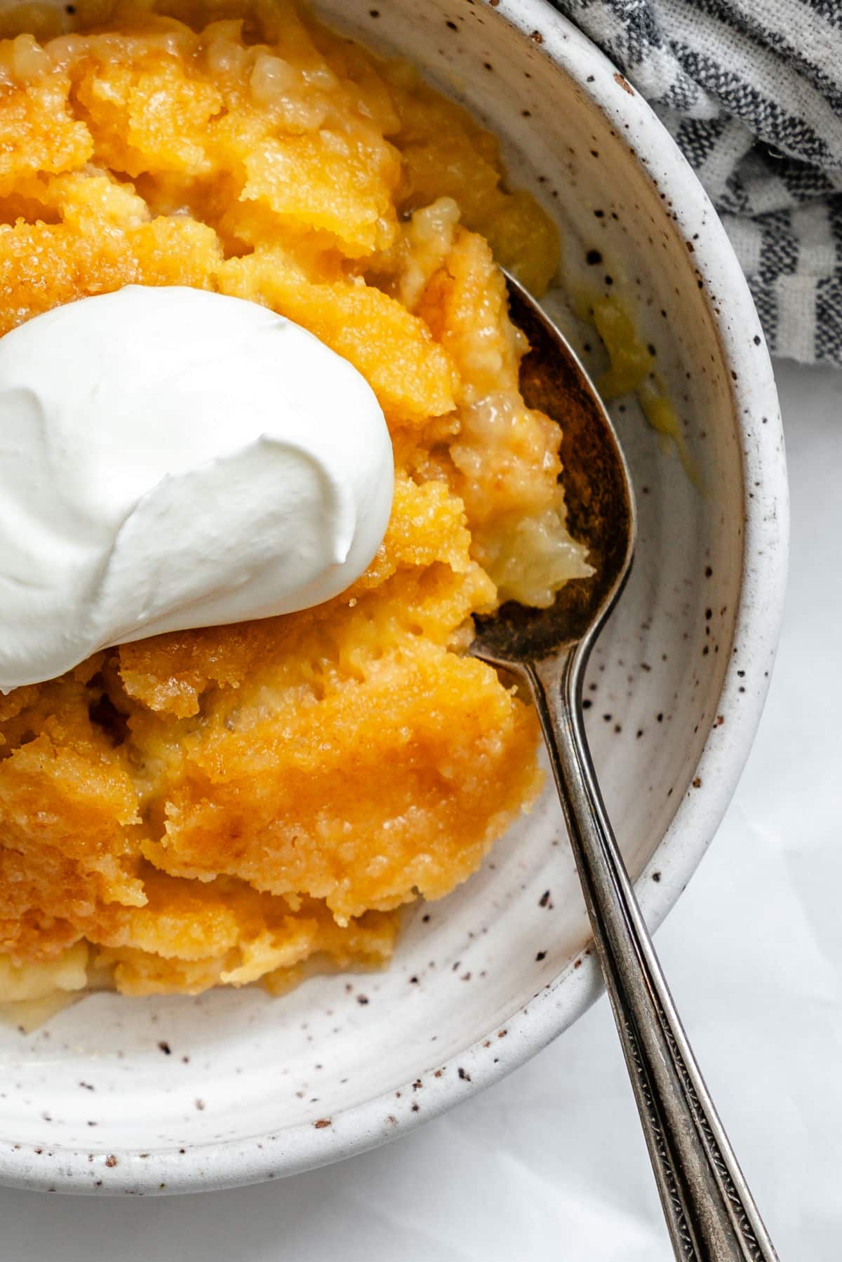 A bowl of pineapple dump cake topped with a dollop of whipped cream.