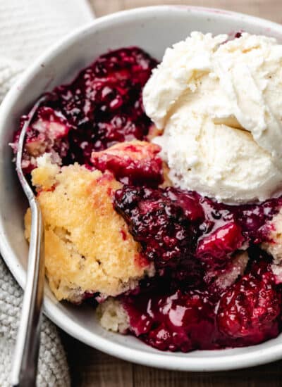 A silver spoon in a bowl of blackberry cobbler.