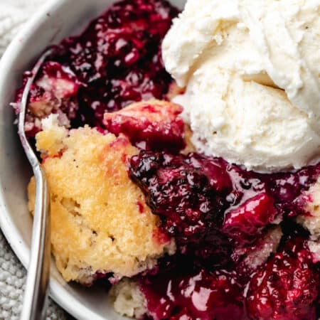 A silver spoon in a bowl of blackberry cobbler.