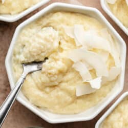 A ramekin with coconut rice pudding with a spoon holding a scoop of pudding.