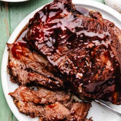 A plate of partially sliced slow cooker bbq brisket next to a dish of baked beans.