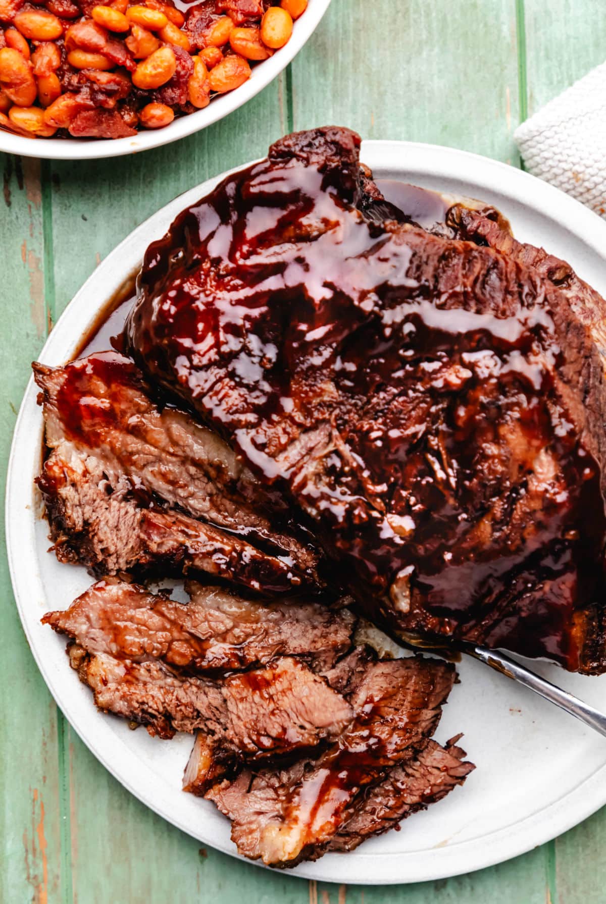 Une assiette de brisket de boeuf barbecue partiellement tranché à côté d'un plat de haricots cuits.
