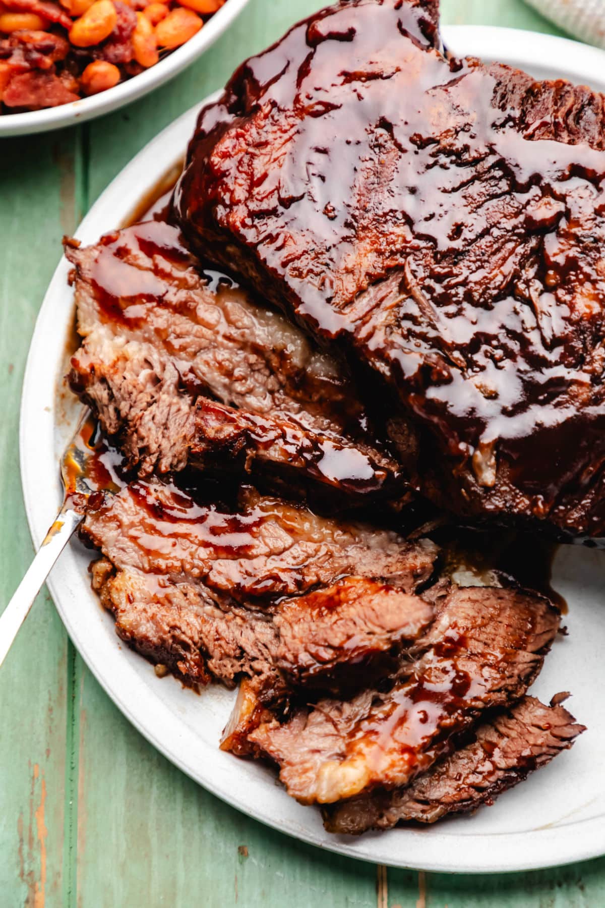 Slices brisket on a white plate with a fork underneath.